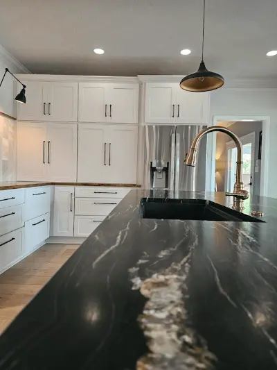Large black marble island with a sink in the middle and white cabinets